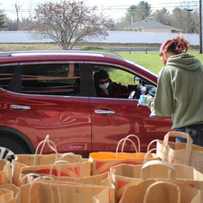 A person takes an order from a maroon SUV with bags of food in foreground