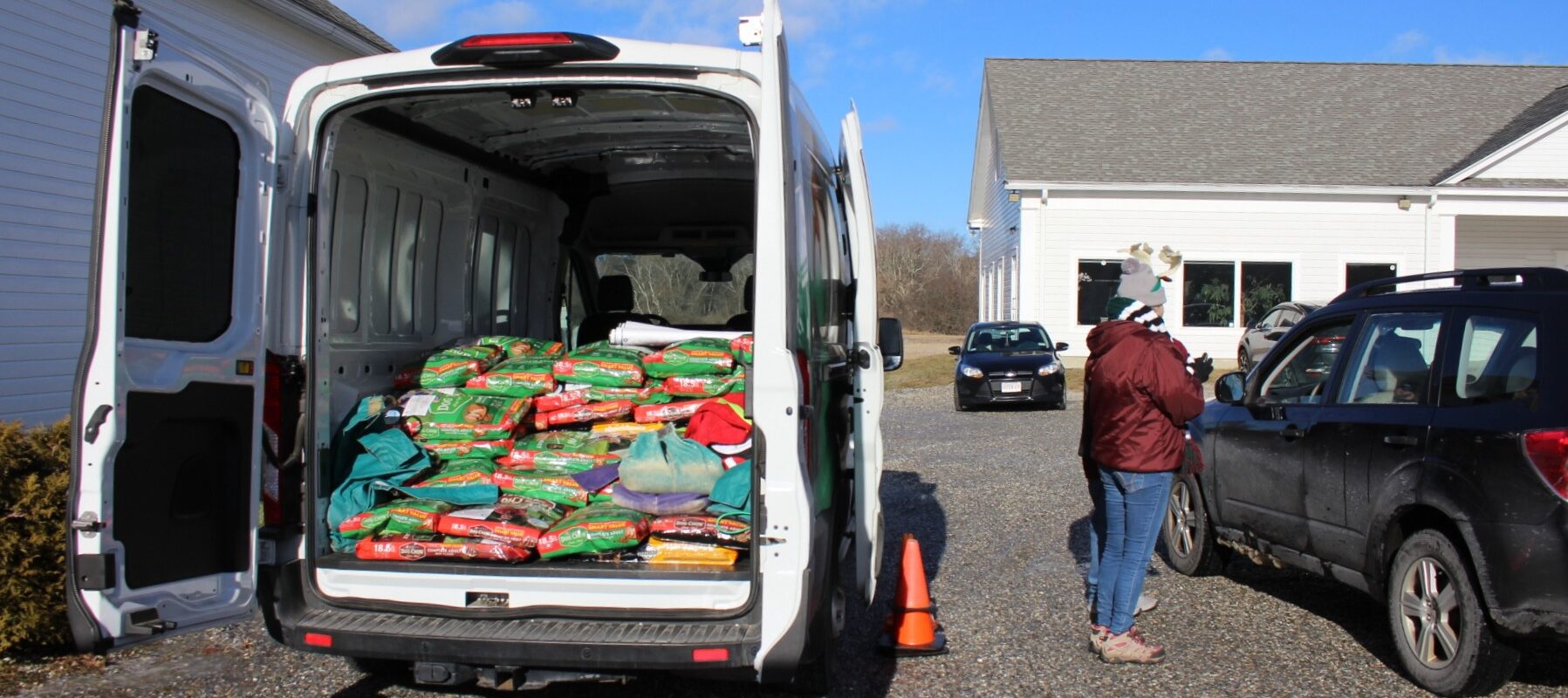 Back of a white van open showing bags of pet food with someone standing next to a vehicle taking an order