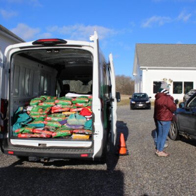Back of a white van open showing bags of pet food with someone standing next to a vehicle taking an order