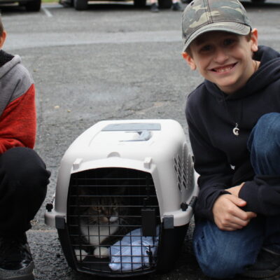 Two boys kneel on either side of a cat in a carrier